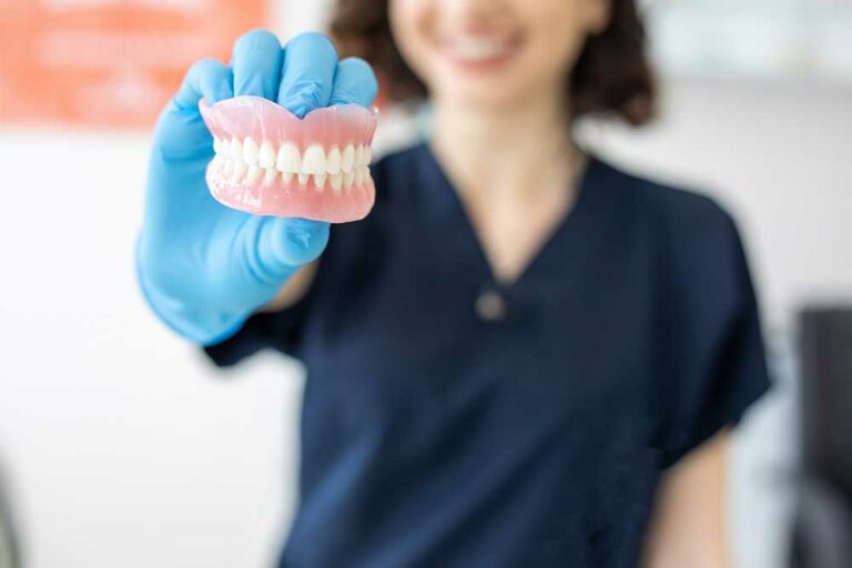 female dentist wearing a blue glove holding dentures