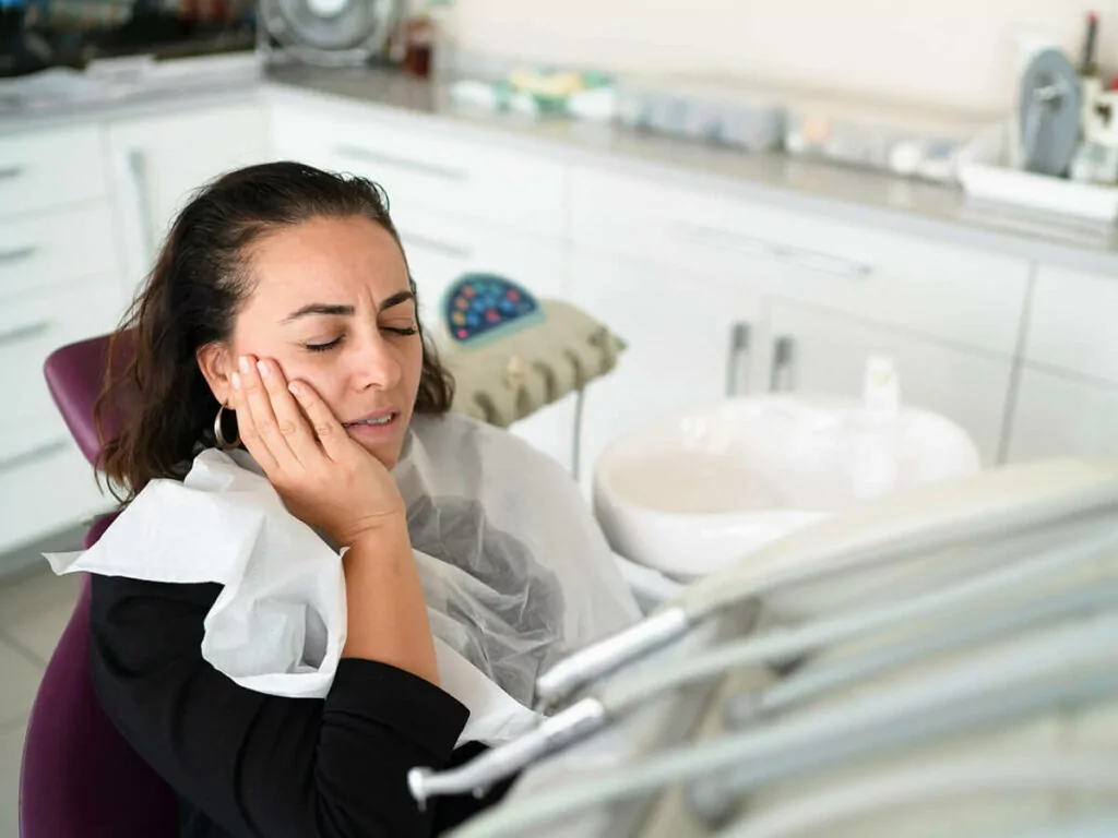A female dental patient holds her mouth in pain while suffering from a dental emergency
